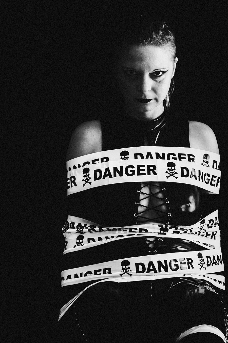 Frau im Latexanzug, um sie gewickelt ein Band mit der Aufschrift "Danger" fotografiert in schwarz/weiss