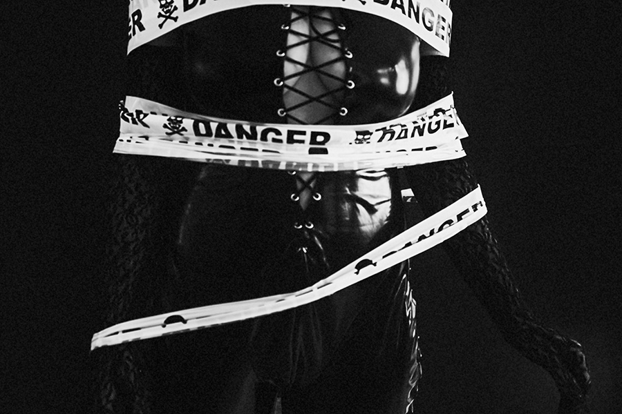 Frau im Latexanzug, um sie gewickelt ein Band mit der Aufschrift "Danger" fotografiert in schwarz/weiss