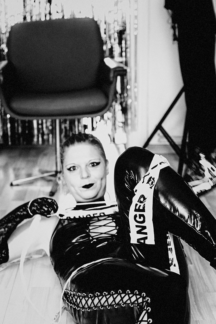 Frau im Latexanzug, um sie gewickelt ein Band mit der Aufschrift "Danger" fotografiert in schwarz/weiss