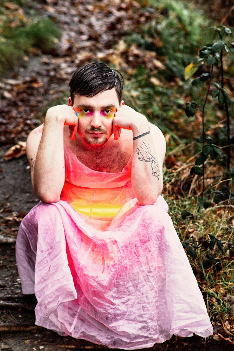 Person im rosa Kleid hält ein rot leuchtendes Objekt auf einem herbstlichen Waldweg; dramatische, kunstvolle Bildstimmung.