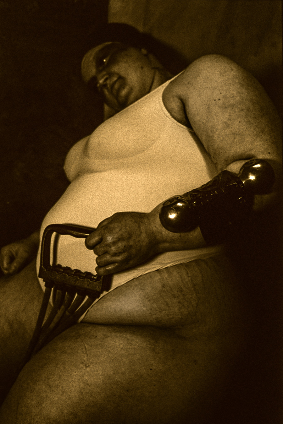 Analoge Schwarzweißaufnahme einer sitzenden Person mit Hantel, aufgenommen aus niedriger Perspektive.