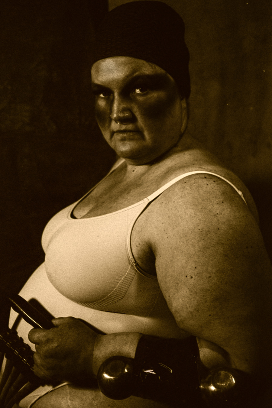 Analoge Schwarzweißaufnahme einer Person mit Hantel, die seitlich posiert und selbstbewusst in die Kamera blickt.