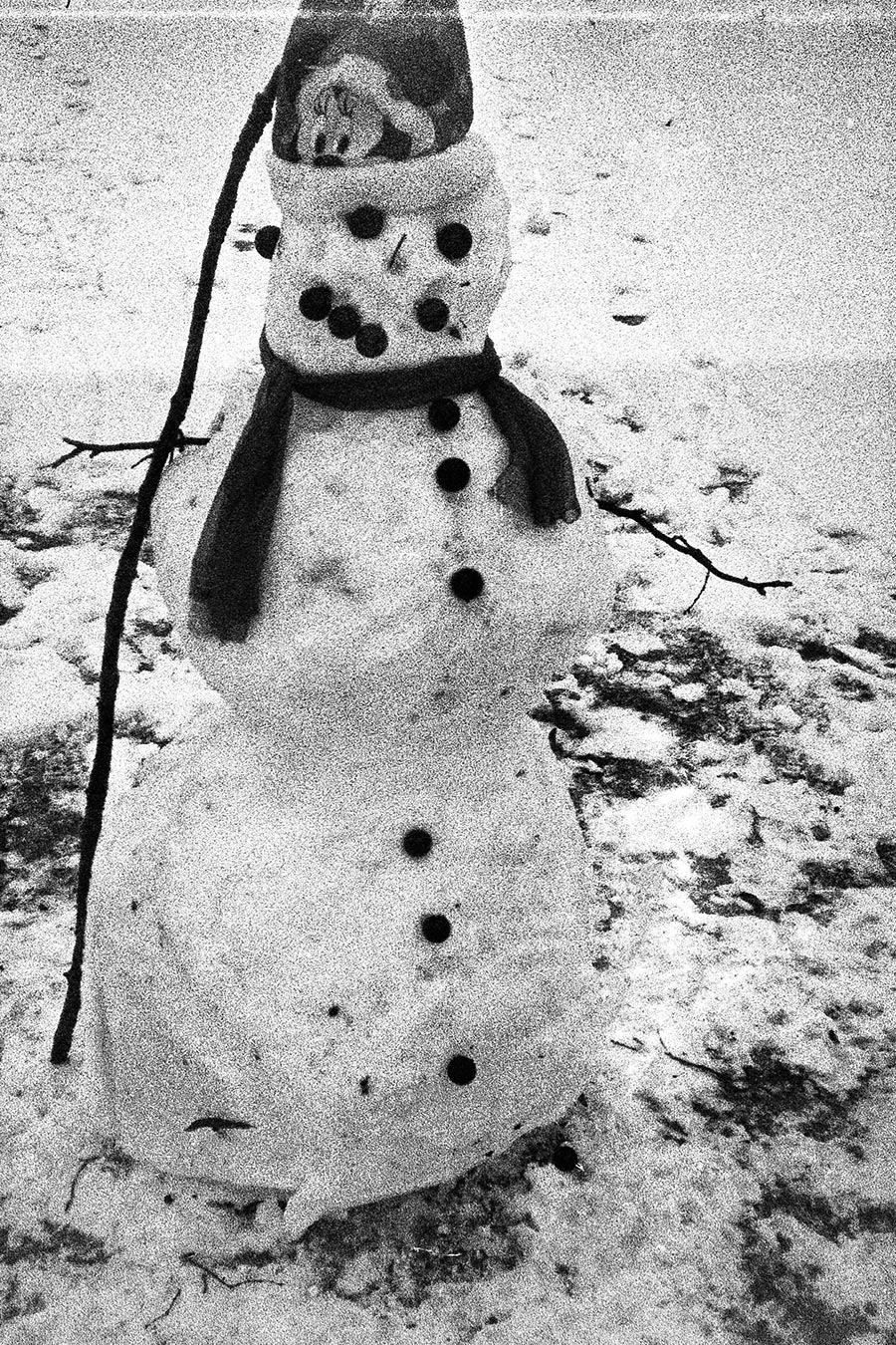 Schwarzweißfotografie eines Schneemanns mit Stockarmen und Schal im Schnee