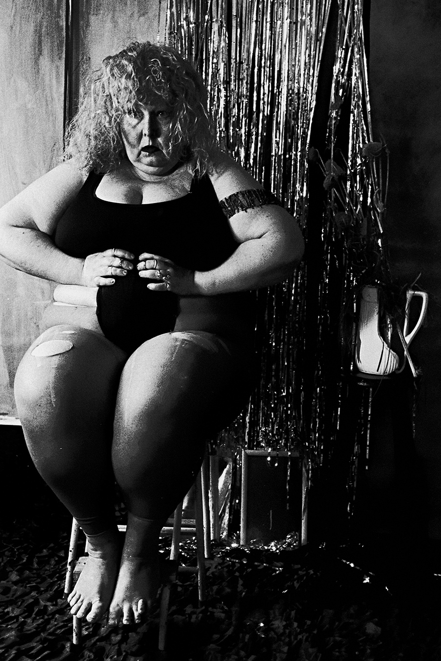 Schwarz-weiß Selbstporträt einer Frau auf Stuhl vor glänzendem Lametta-Vorhang, digital-analog Remix