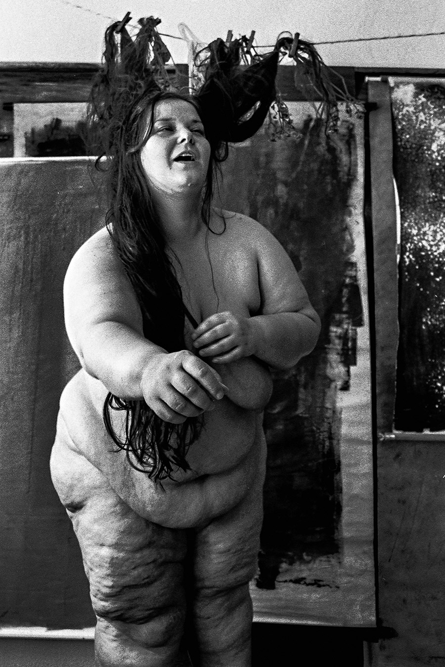 Nackte dicke Frau steht mit verschränkten Armen, Kopf zurückgeworfen, Haare an der Leine, analoges Schwarz-Weiß-Foto auf Kodak T-Max 100, Serie „Der Ballast"
