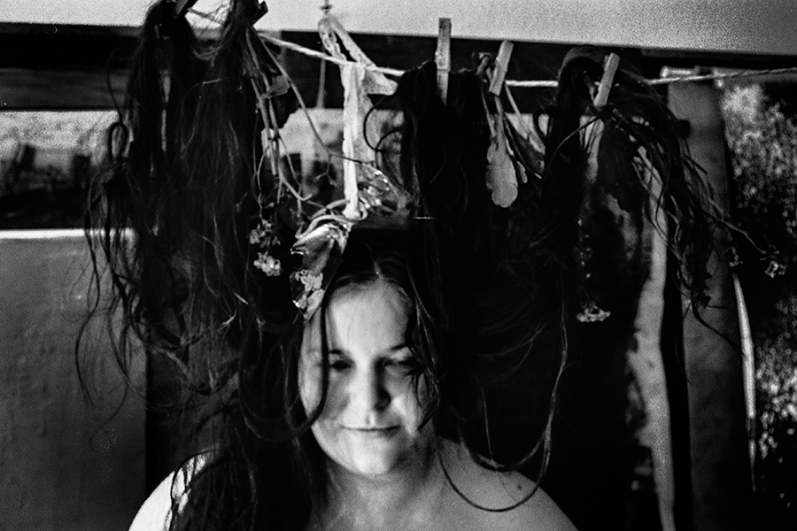 Frau mit Haaren und getrockneten Blumen an einer Wäscheleine über dem Kopf, Blick nach unten, analoges Schwarz-Weiß-Foto auf Kodak T-Max 100, Serie „Der Ballast"
