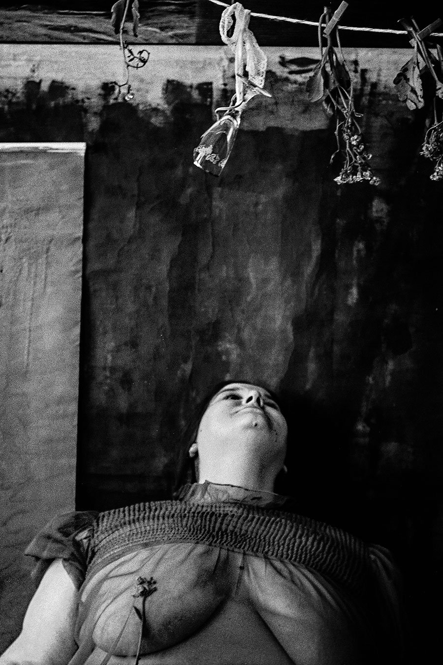 Dicke Frau in transparentem Kleid liegt zurückgelehnt, Kopf nach hinten gestreckt, welke Blumen hängen über ihr, analoges Schwarz-Weiß-Foto auf Kodak T-Max 100, Serie „Der Ballast"