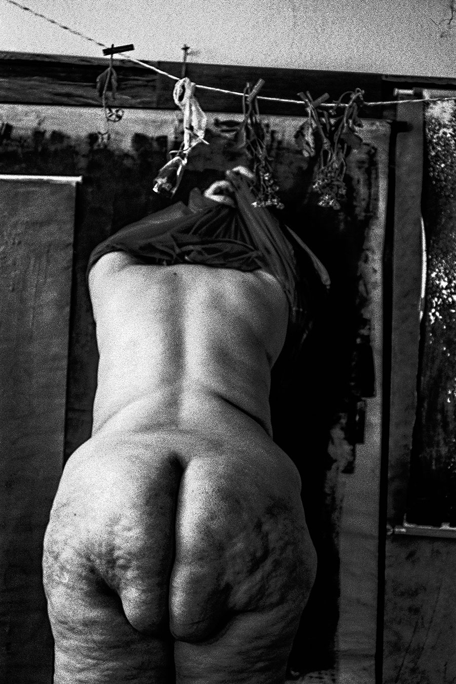 Nackter weiblicher dicker Rücken, Stoff über dem Kopf, Leine mit welken Blumen oben, analoges Schwarz-Weiß-Foto auf Kodak T-Max 100, Serie „Der Ballast"
Beschreibung: Rückenansicht aus nächster Nähe. 
