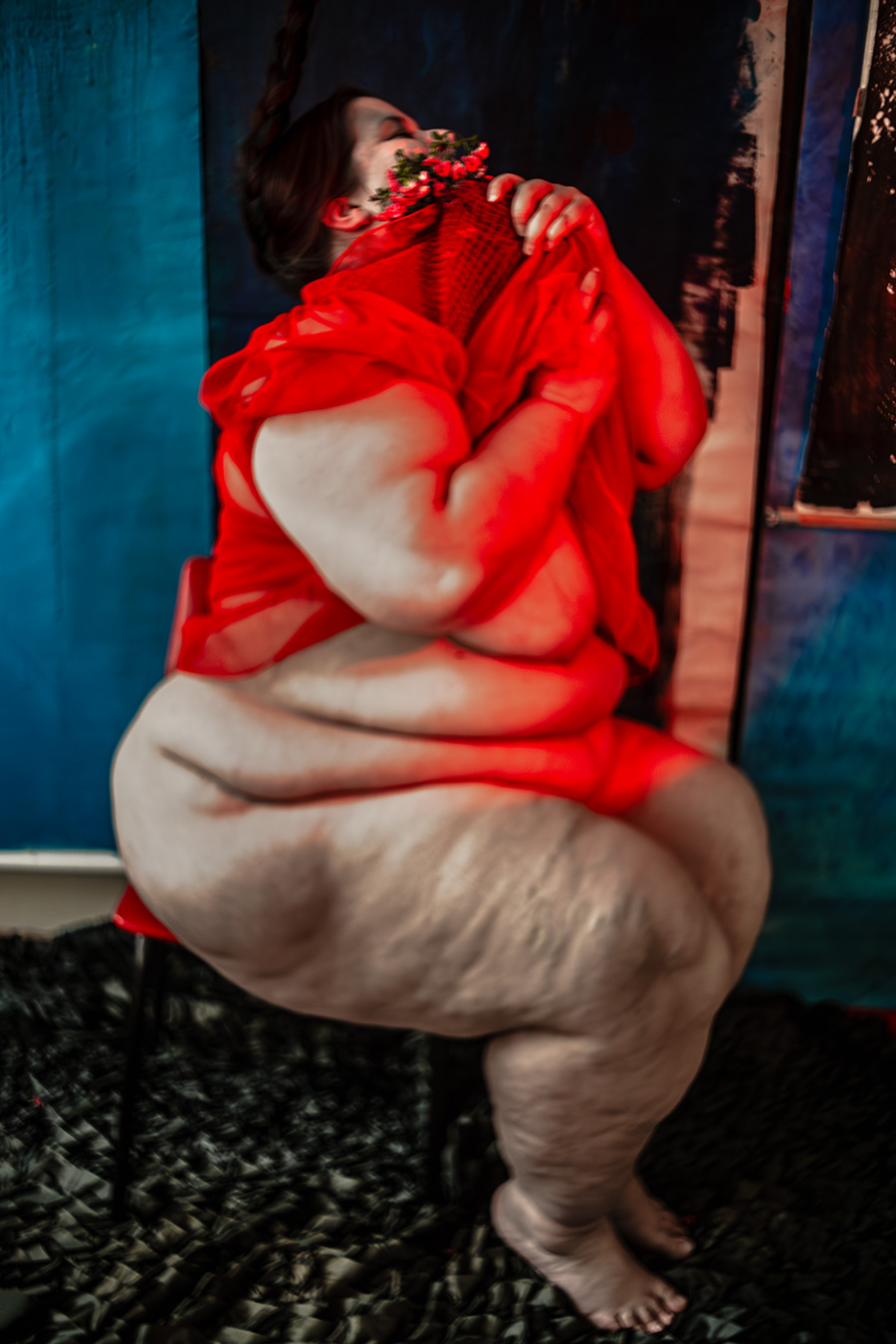 Frau in rotem Kleid hält Blumen ans Gesicht, Zopf seitlich, blauer Hintergrund, Serie „Der Ballast"