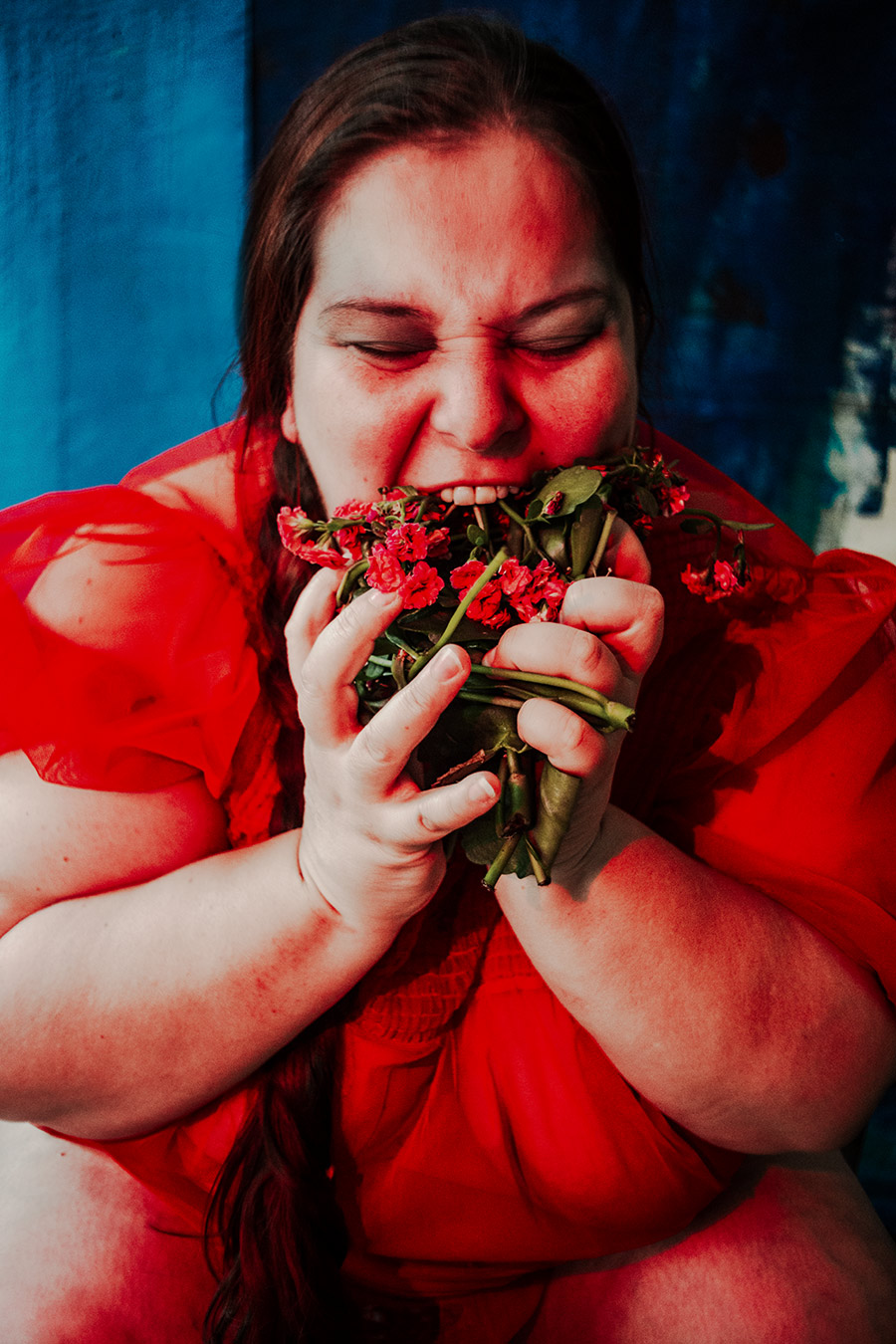 Frau in rotem Kleid beißt in einen großen welken Blumenstrauß, blauer und weißer Hintergrund, Serie „Der Ballast"