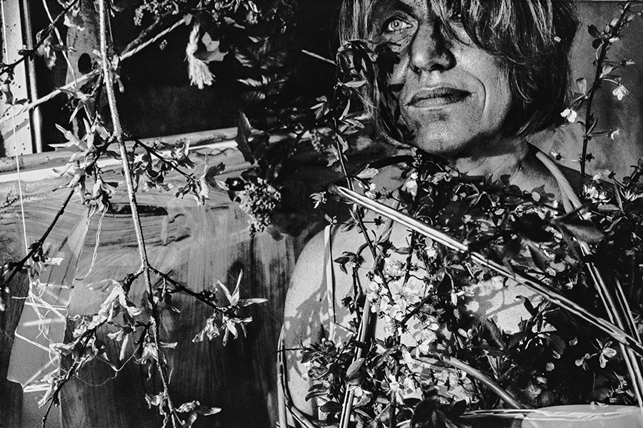 Greisenmädchen Teil 2, Frau mit Make-up lächelt direkt in die Kamera, umgeben von Blüten, Fomapan 400 Ortho, Fotografin Leipzig