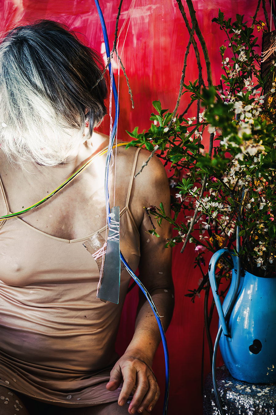 Fotokunst Greisenmädchen, Frauenkörper mit Metallplatte und Kabeln, blaue Emaillekanne mit Blütenzweigen, Fotografin Leipzig