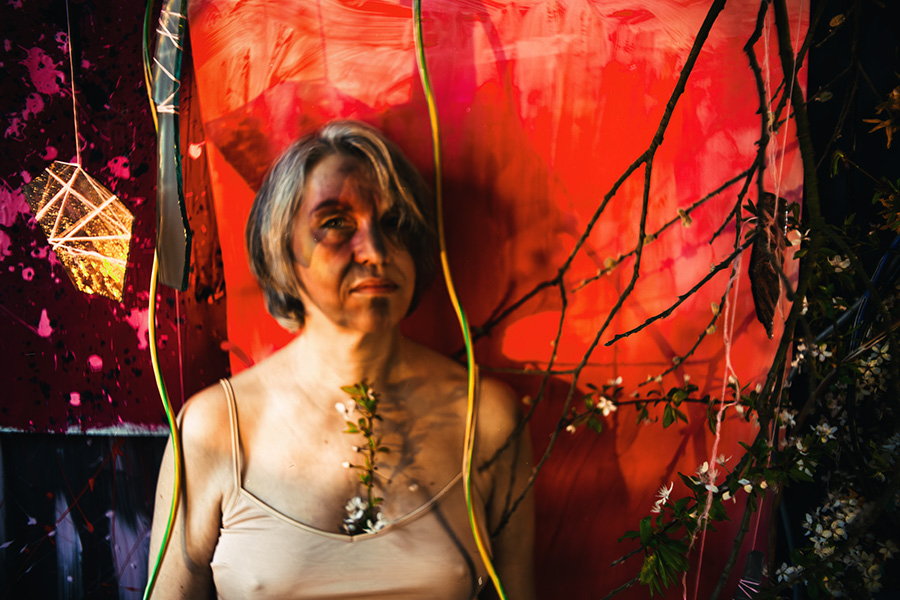 Fotokunst Greisenmädchen, ältere Frau frontal mit ernstem Blick, Blütenzweig auf der Brust, leuchtendes Objekt links, Fotografin Leipzig