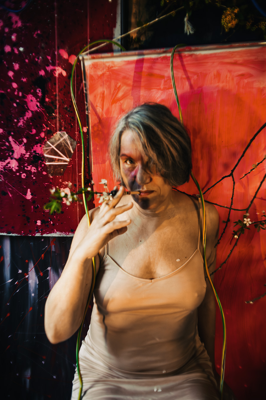 Fotokunst Greisenmädchen, Frau mit blauem Make-up hält Blütenzweig vor den Mund, schaut direkt in die Kamera, Fotografin Leipzig