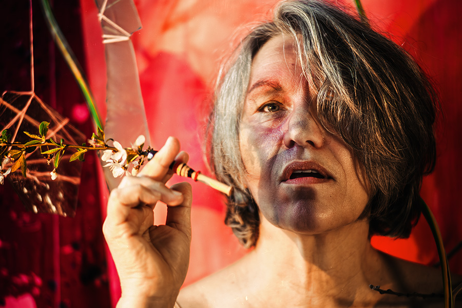 Fotokunst Greisenmädchen, ältere Frau hält zarten Blütenzweig mit Zigarettenspitze, intensive Lichtschatten auf dem Gesicht, Fotografin Leipzig