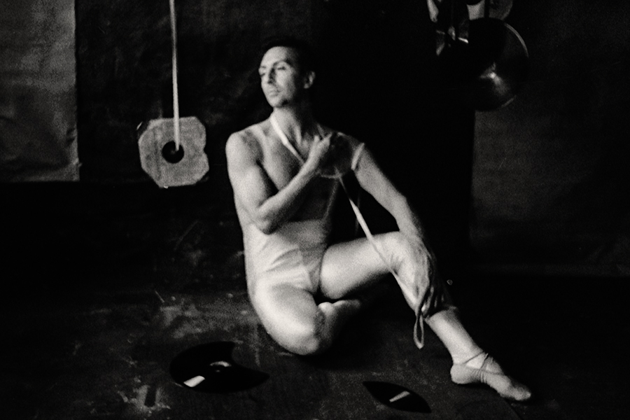 Fomapan 400 gepusht · Zenit, Schwarzweißfoto: Mann in weißem Balletttrikot sitzt auf dem Boden, Schnur läuft über seine Brust, Blick zur Seite, Spitzenschuhe, Schallplatten um ihn herum.