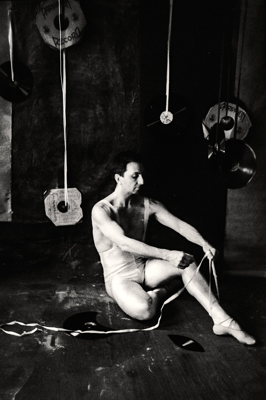 Fomapan 400 gepusht · Zenit, Mann in weißem Balletttrikot sitzt auf dem Boden und bindet seinen Spitzenschuh, Schallplatten hängen im Raum, weiches körniges Licht.