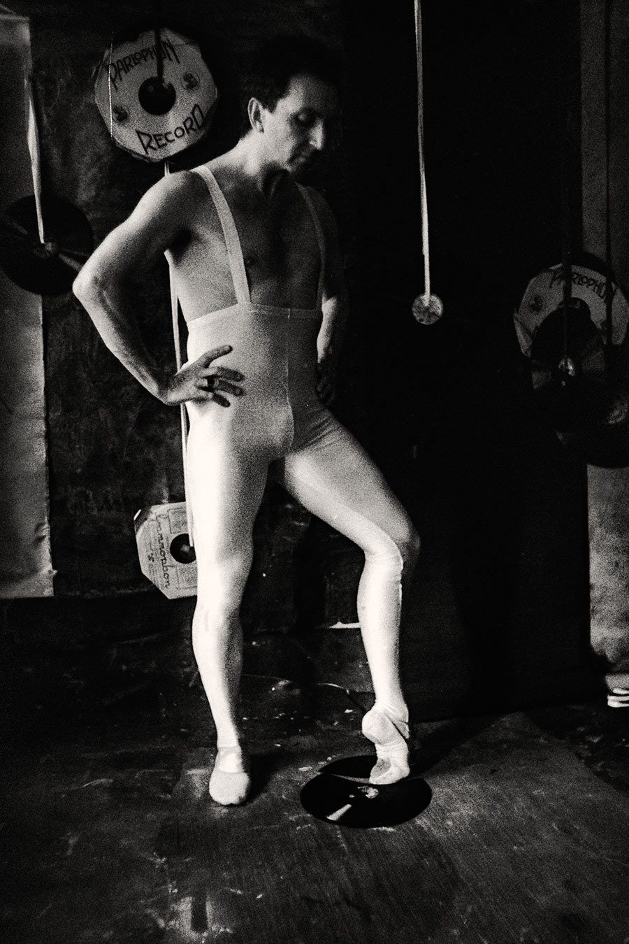 Fomapan 400 gepusht · Zenit, Schwarzweißfoto: Mann in weißem Balletttrikot steht seitlich, eine Hand an der Hüfte, Fuß auf einer Schallplatte, Blick nach unten, Schallplatten im Hintergrund.