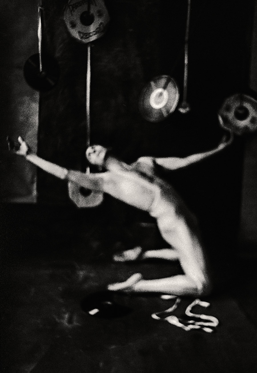 Fomapan 400 gepusht · Zenit, Stark gekörntes Schwarzweißfoto: Tanzender nackter Körper zwischen hängenden Schallplatten, Arme weit ausgestreckt, Bewegungsunschärfe, fast abstrakt.
