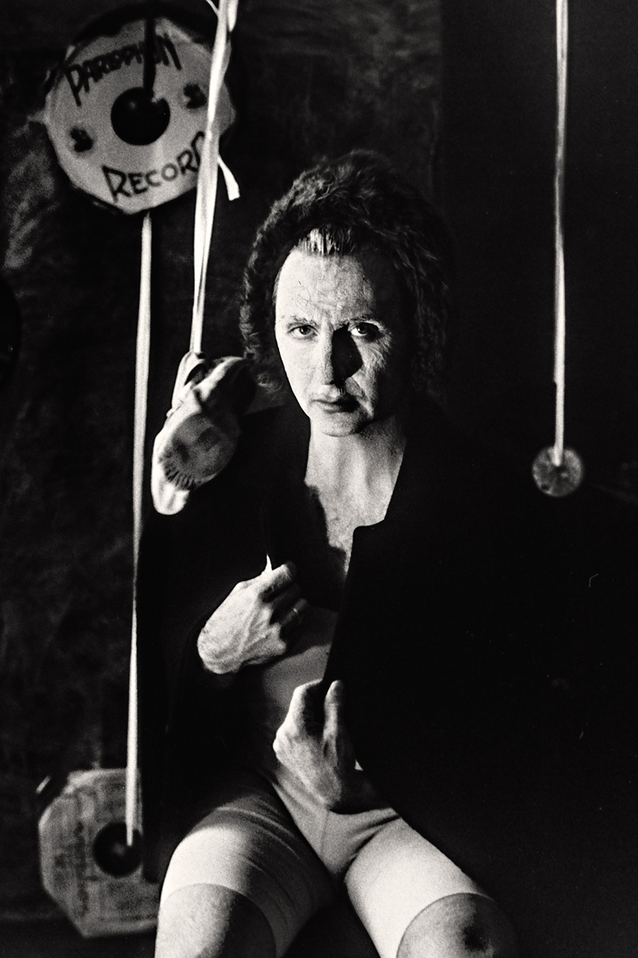 Tmax 100 auf 800 gepusht, analoge Fotografie Leipzig, Mann in dunklem Oberteil sitzt, Hände in Bewegung, direkter intensiver Blick in die Kamera, Schallplatten und Schnüre im Hintergrund.