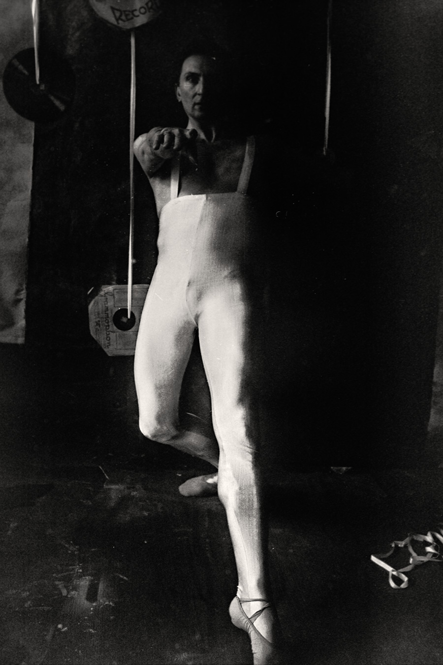 Fomapan 400 gepusht · Zenit, analoges Schwarzweißfoto: Mann in weißem Trikot steht, ein Bein angehoben, greift mit beiden Händen nach einer Schallplatte, Gesicht im Schatten.