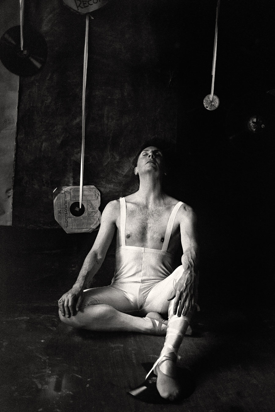 Fomapan 400 gepusht · Zenit, analoge fotografie,Schwarzweißfoto: Mann in weißem Balletttrikot sitzt auf dem Boden, Kopf zurückgelegt, Augen geschlossen, Spitzenschuhe, Schallplatten im Hintergrund.