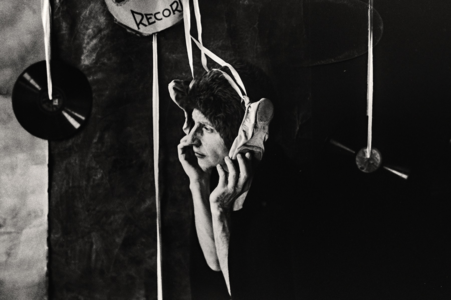 Tmax 100 auf 800 gepusht, analoge Fotografie Leipzig, balett, Schwarzweißfoto: Mann hält Spitzenschuh nah an sein Gesicht, Hände umfassen ihn zärtlich, nachdenklicher Blick, Schallplatten und Schnüre im Hintergrund.