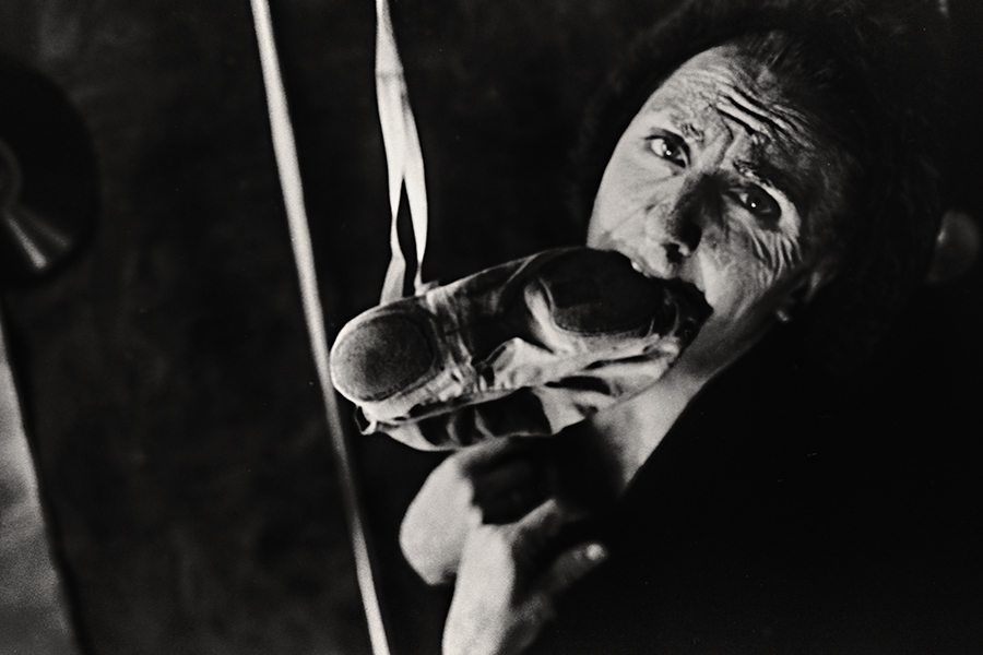 Tmax 100 auf 800 gepusht, analoge Fotografie Leipzig, Nahaufnahme, Mann hält Spitzenschuh nah am Gesicht, Blick nach oben, gealterte Züge, starkes Korn, dunkler Hintergrund.