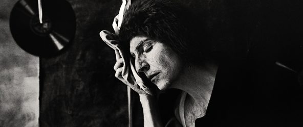 Tmax 100 auf 800 gepusht, analoge Fotografie Leipzig,Schwarzweißfoto: Mann in dunklem Oberteil, Augen geschlossen, Spitzenschuh liegt an der Wange, Hand hält ihn, Kopf geneigt, Schallplatten im Hintergrund.