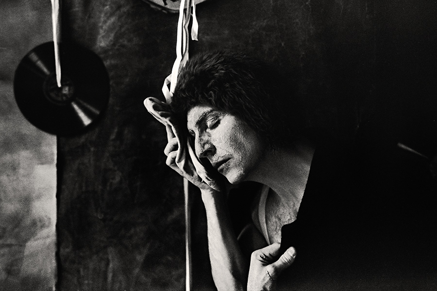 Tmax 100 auf 800 gepusht, analoge Fotografie Leipzig,Schwarzweißfoto: Mann in dunklem Oberteil, Augen geschlossen, Spitzenschuh liegt an der Wange, Hand hält ihn, Kopf geneigt, Schallplatten im Hintergrund.