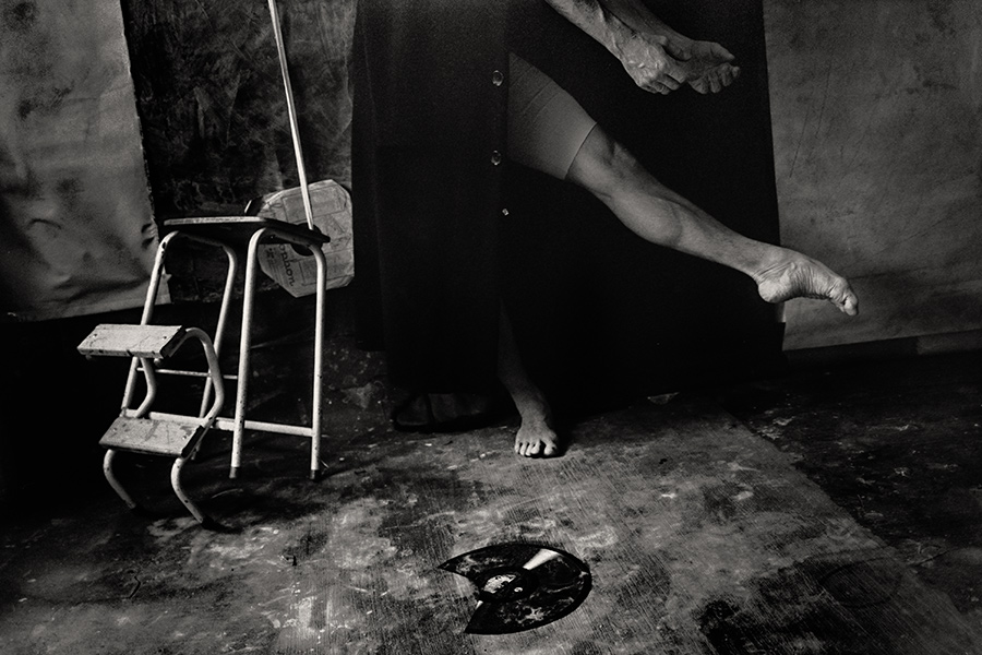 Tmax 100 auf 800 gepusht, analoge Fotografie Leipzig, Schwarzweißfoto: Ausschnitt, gealterte Beine und Fuß strecken sich aus, ein Bein erhoben, Hocker leer daneben, Schallplatte auf dem Boden, schwarzer Mantel.