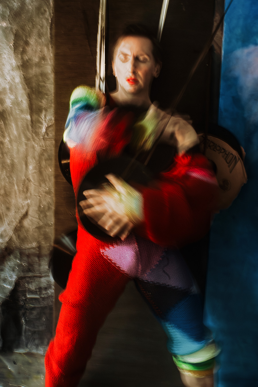 Farbfoto mit Bewegungsunschärfe: Mann in rotem Strickanzug zwischen zwei Wänden eingeklemmt, Augen geschlossen, Arme in Bewegung, rote Lippen.