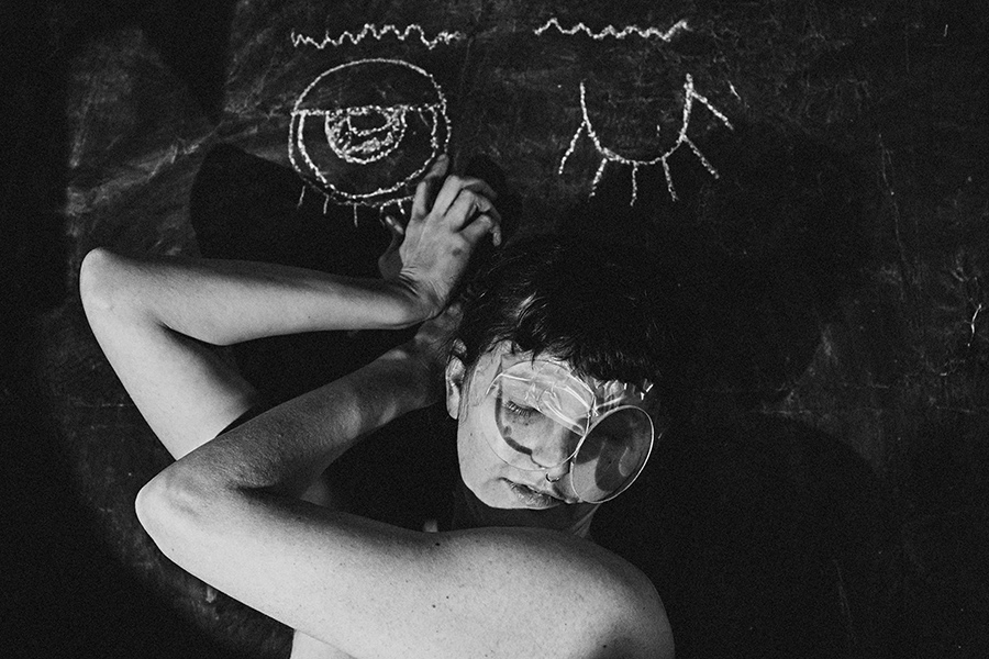 Trachom Fotokunst, Frau liegend mit Lupe auf dem Gesicht vor Kreideaugen auf schwarzer Tafel, Fotografin Leipzig, Antje Kröger
