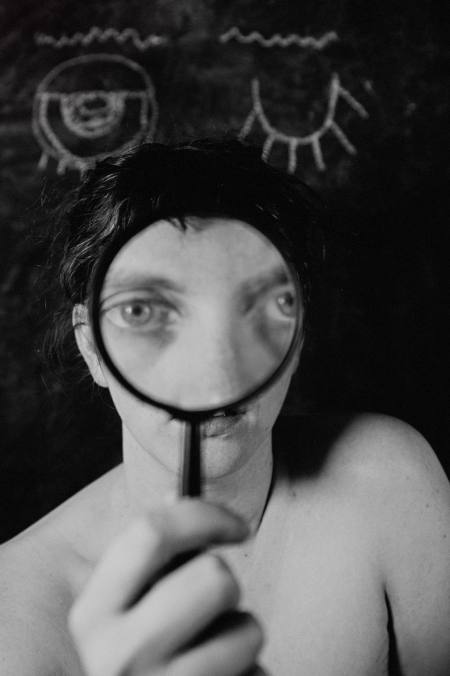Trachom Fotokunst, Frau hält Lupe vor den Mund, Augen schauen über das Glas, Kreideaugen auf schwarzer Tafel, Fotografin Leipzig
