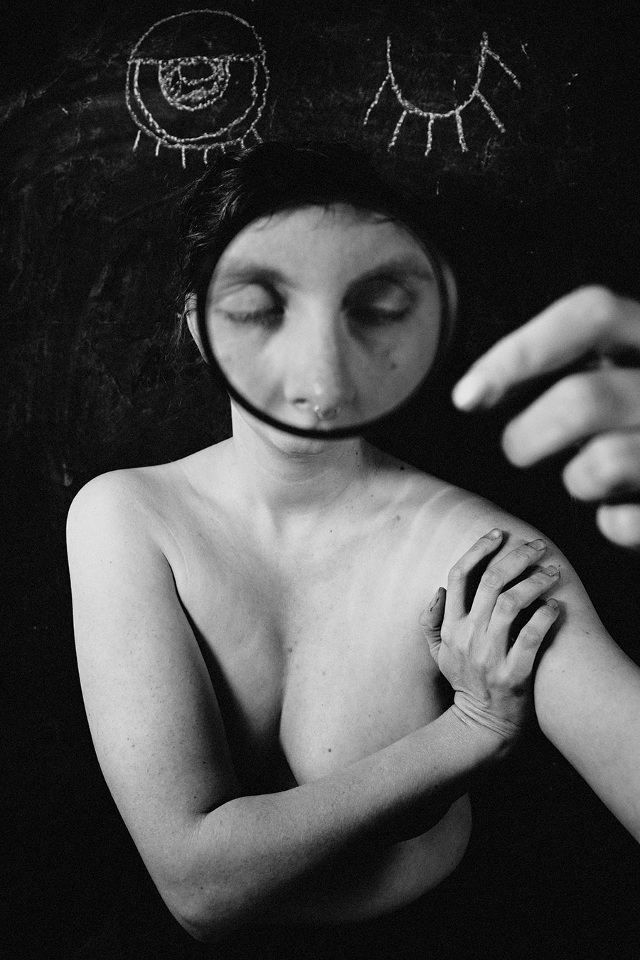 Trachom Fotokunst, Frau mit Lupe vor geschlossenem Gesicht und Händen auf der Schulter vor Kreideaugen, Fotografin Leipzig
