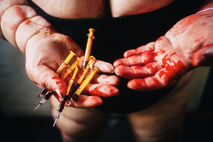 Zwei Hände halten blutbeschmierte Spritzen wie eine Darbietung, eine Handfläche vollständig mit Blut bedeckt – politische Fotokunst Antje Kröger Leipzig, Serie Mehrenge