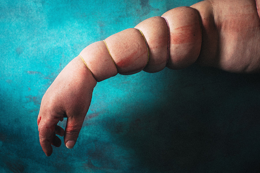 Arm senkrecht hängend, von Gummibändern gleichmäßig eingeschnürt, Haut quillt hervor, Hand schlaff und livide – inszenierte Körperfotografie Antje Kröger Berlin Leipzig, Serie Mehrenge