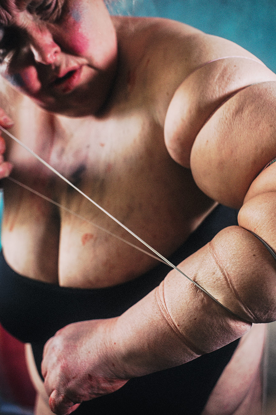 Nahaufnahme nackter Oberkörper von oben mit diagonal gespanntem Gummiband über Brust und Arm – künstlerische Körperfotografie Antje Kröger Leipzig, Serie Mehrenge