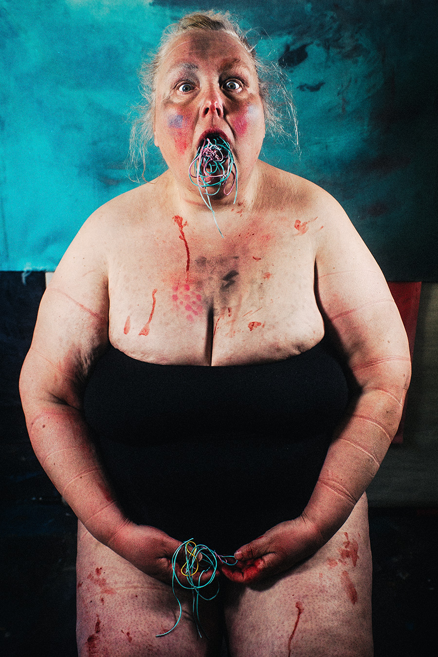 Ganzkörper frontal, Gummibänder quellen aus weit geöffnetem Mund, Blutspuren auf Haut und Beinen, Druckspuren eingeschnürter Arme – politische Körper-Fotokunst Antje Kröger Leipzig, Serie Mehrenge