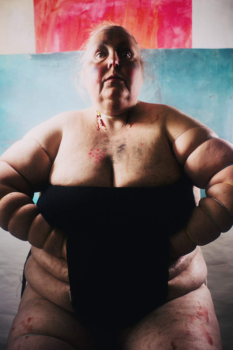 Frontales Ganzkörper-Selbstporträt mit weit ausgebreiteten eingeschnürten Armen, Blick nach oben, gemaltes Kreuz im Hintergrund – politische Körperkunst Antje Kröger Berlin Leipzig, Serie Mehrenge