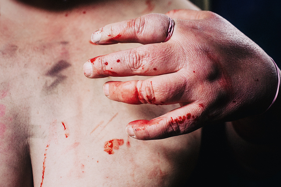 Hand drückt sich in nackte Brust, Blut auf Fingern und Haut, Blitz-Tattoo sichtbar, dramatisches Seitenlicht – körperliche Fotokunst Antje Kröger Berlin, Serie Mehrenge