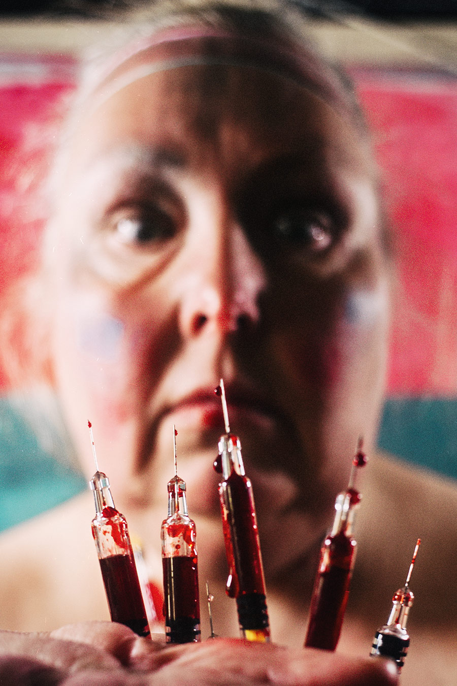  Fünf blutbeschmierte Spritzen in die Kamera gehalten, dahinter unscharf das Gesicht der Fotografin – konzeptuelle Selbstporträt-Fotografie Antje Kröger Leipzig Berlin, Serie Mehrenge