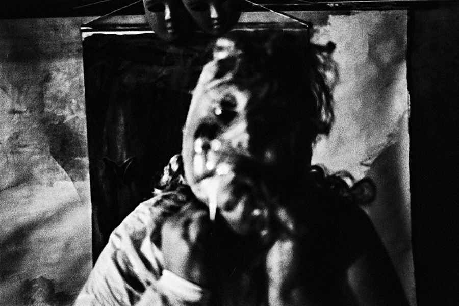 analoge fotokunst leipzig, Analogfoto auf Fomapan 400 Ortho, um eine Stufe gepusht, extrem körnig und stark überbelichtet. Das Gesicht einer dicken Frau ist durch einen überlagerten weißen Lichtkegel fast vollständig ausgelöscht. Im Hintergrund eine schwarze Maske, kaum erkennbar.