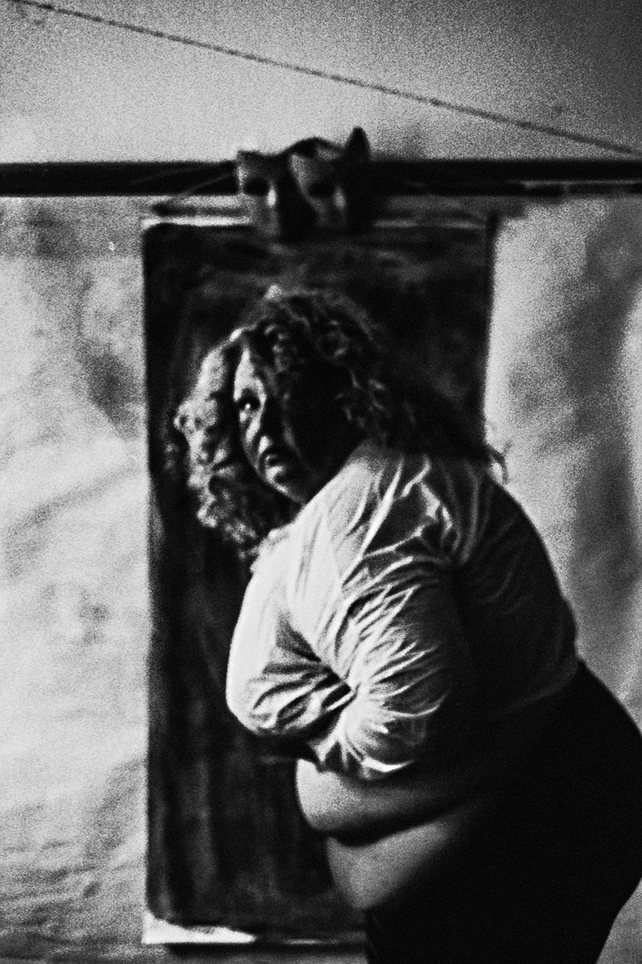 Analogfoto auf Fomapan 400 Ortho, um eine Stufe gepusht, stark körnig. Eine dicke Frau mit Lockenmähne, den Kopf weit zurückgeworfen, die Kehle freigelegt. Das weiße Plastikgewand ist geöffnet, der runde Bauch sichtbar. 