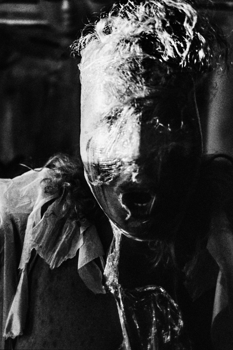 analoge fotokunst leipzig, Analogfoto auf Fomapan 400 Ortho, um eine Stufe gepusht, stark körnig. Extreme Nahaufnahme eines Gesichts, das vollständig mit weißem Material – Stoff, Gaze, Folie – umwickelt ist. Der Mund ist geöffnet wie in einem lautlosen Schrei. Das verfilzte Haar ist mit dem weißen Material verwoben.