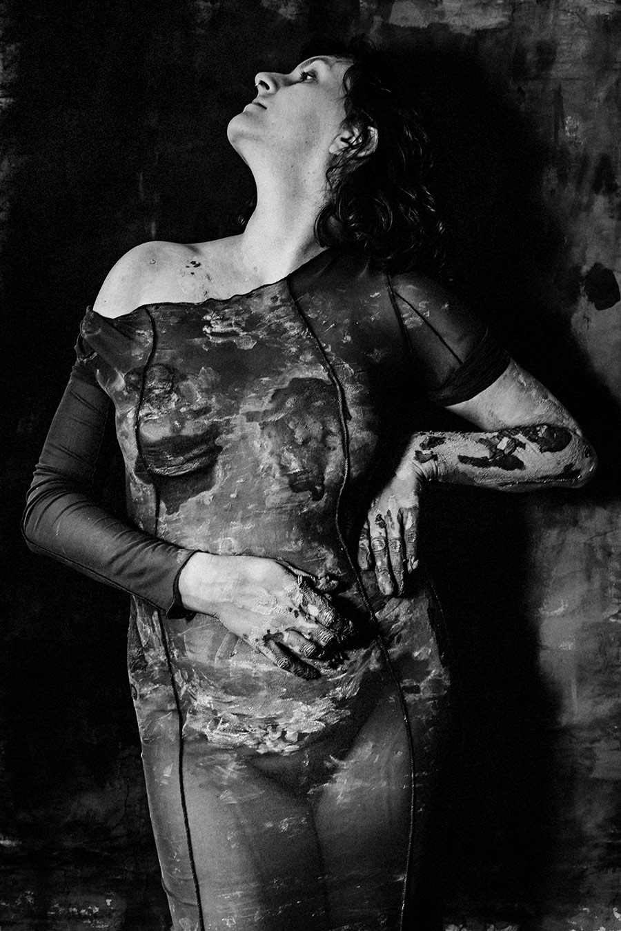 Frau im tonbedeckten Kleid, Kopf weit in den Nacken geworfen, Blick nach oben, Hände an den Körper gepresst.