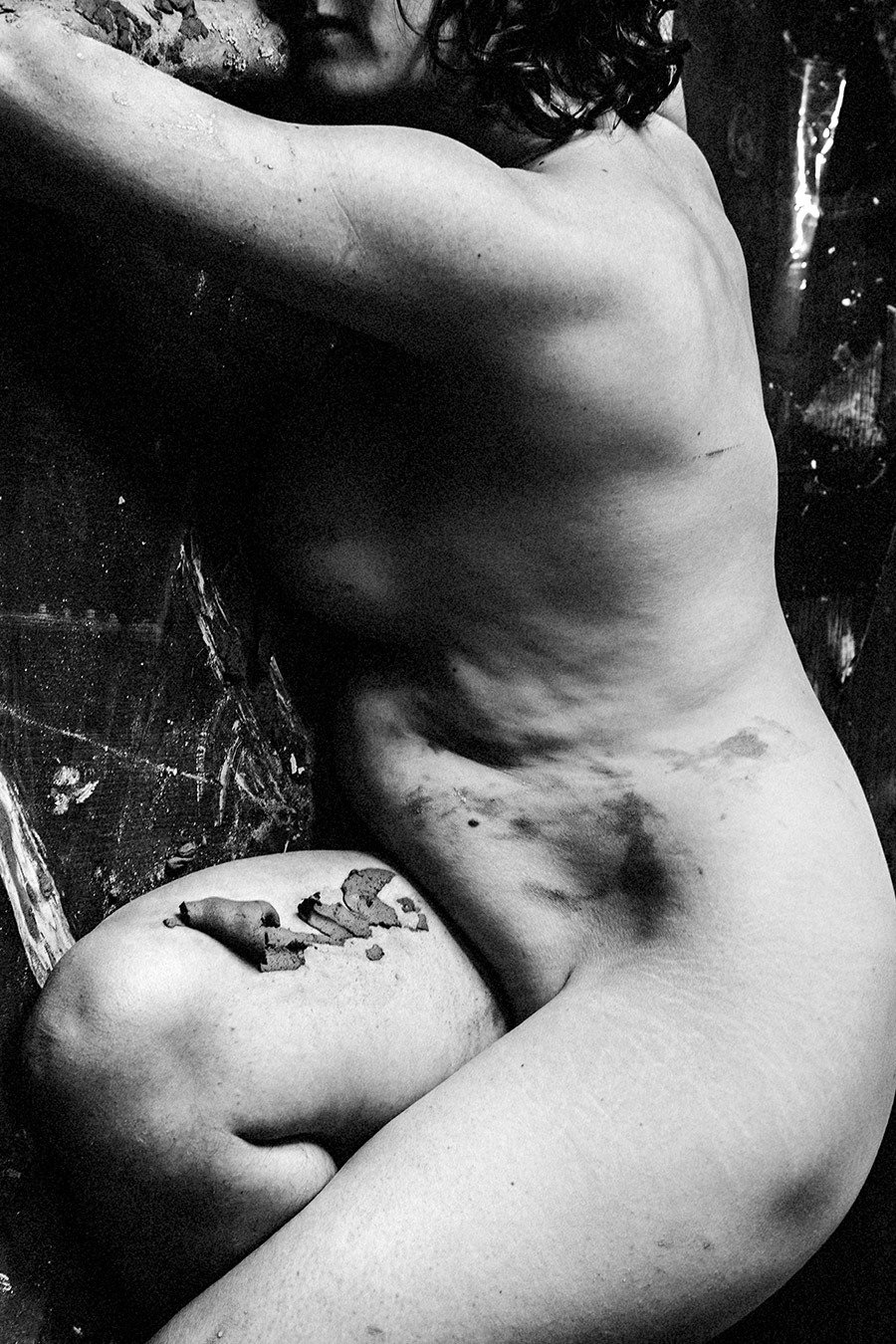 Schwarzweißfoto: Ausschnitt von Rücken, Hüfte und Oberschenkel einer Frau, Ton und abbröckelnde Farbe auf der Haut.