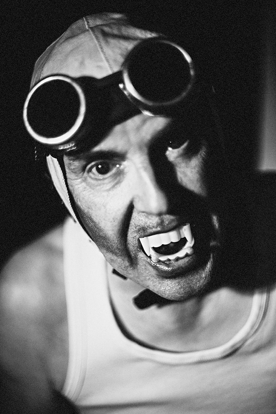 Schwarzweißporträt: Mann mit Schweißerbrille, Lederkappe und Vampirzähnen, intensiver Blick direkt in die Kamera, starkes Seitenlicht, Nahaufnahme, Fotokunst Antje Kröger