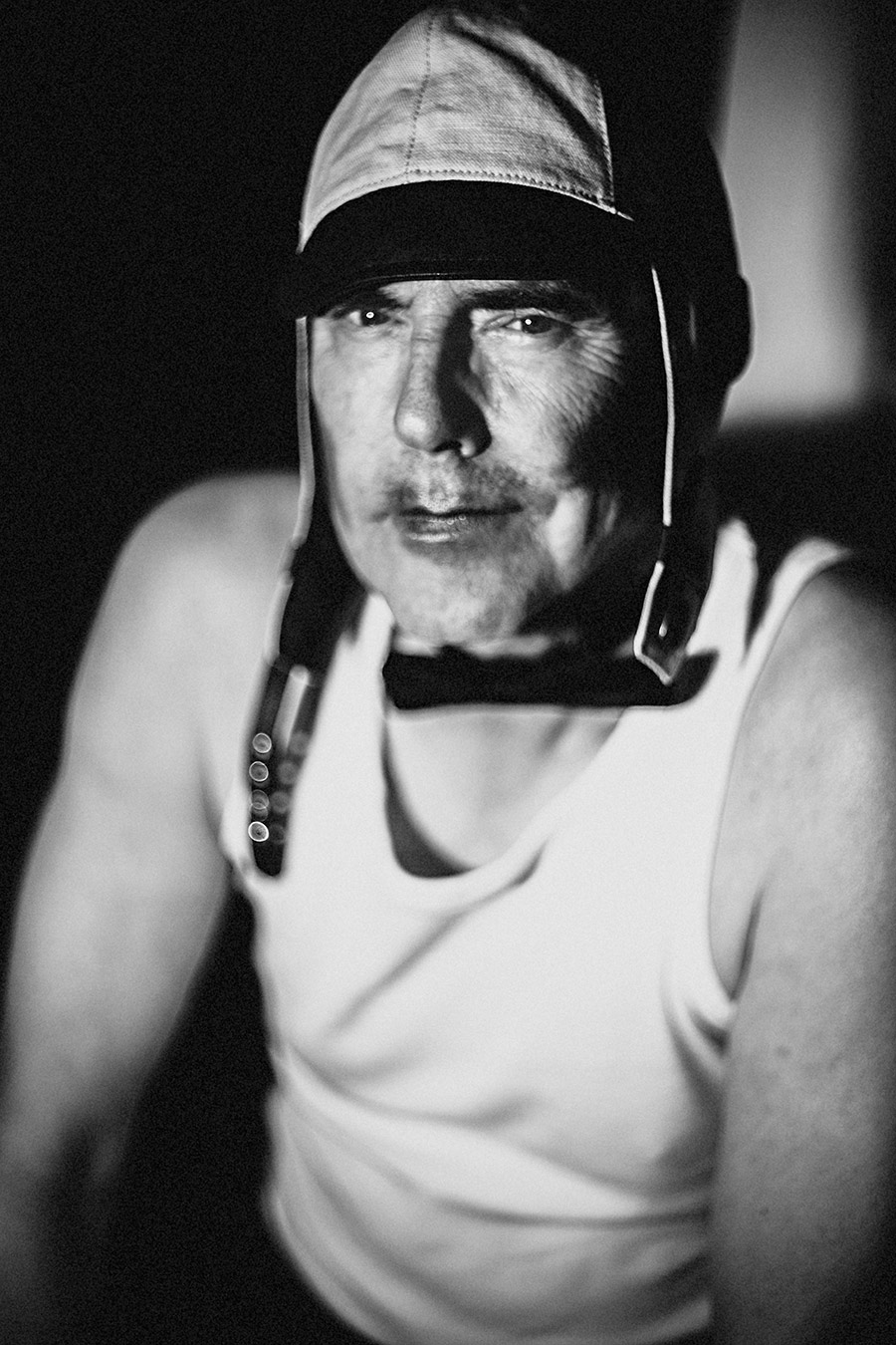 Schwarzweißporträt: Mann mit Lederhelm und Riemenzeug, direkter Blick in die Kamera, Unterhemd, weiches Licht, Fotokunst Antje Kröger