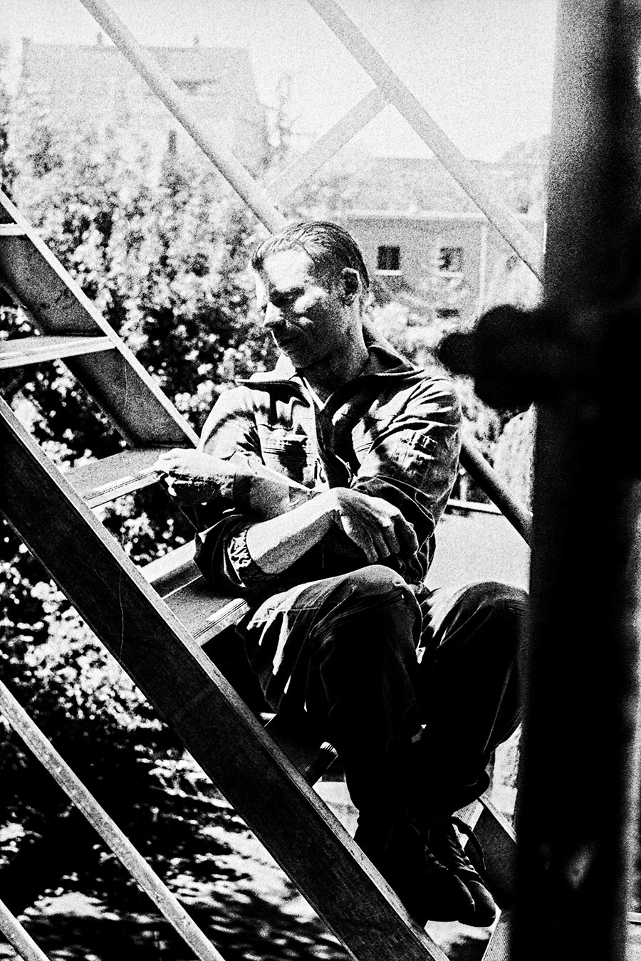 Zenith analog, inszeniertes Schwarzweißfoto, Mann sitzt auf Gerüst, hartes Licht, nachdenkliche Pose, gepushter Film, Stadtlandschaft Hintergrund